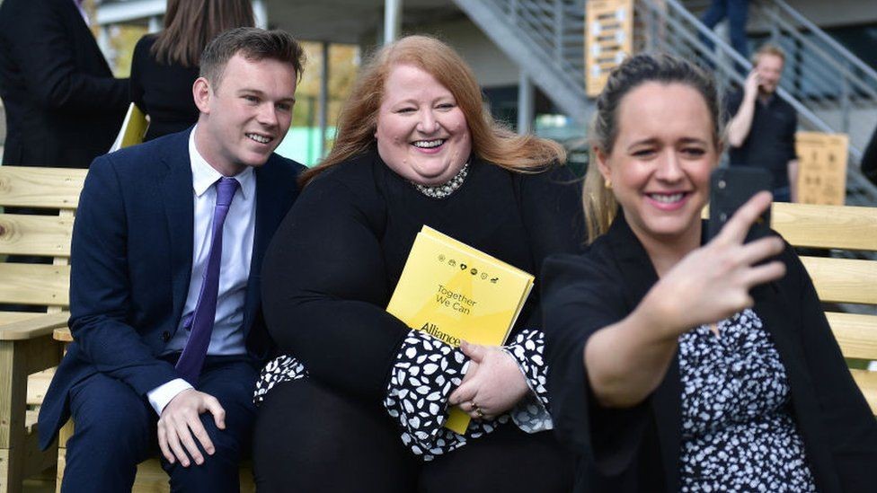 Kate Nicholl (R) takes a selfie photograph of Alliance party leader Naomi Long (C) and fellow party candidates following the Alliance party manifesto launch at CIYMS recreational grounds on April 27, 2022 in Belfast.