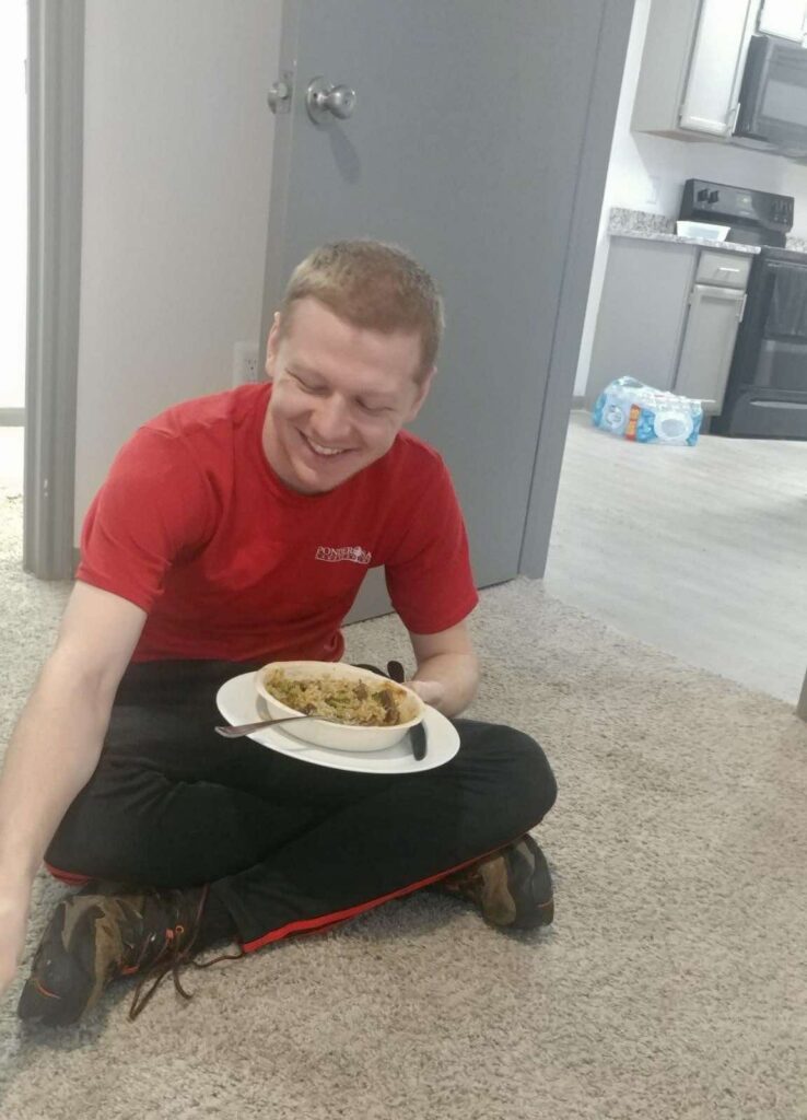A person sitting on the floor with a plate of food

Description automatically generated